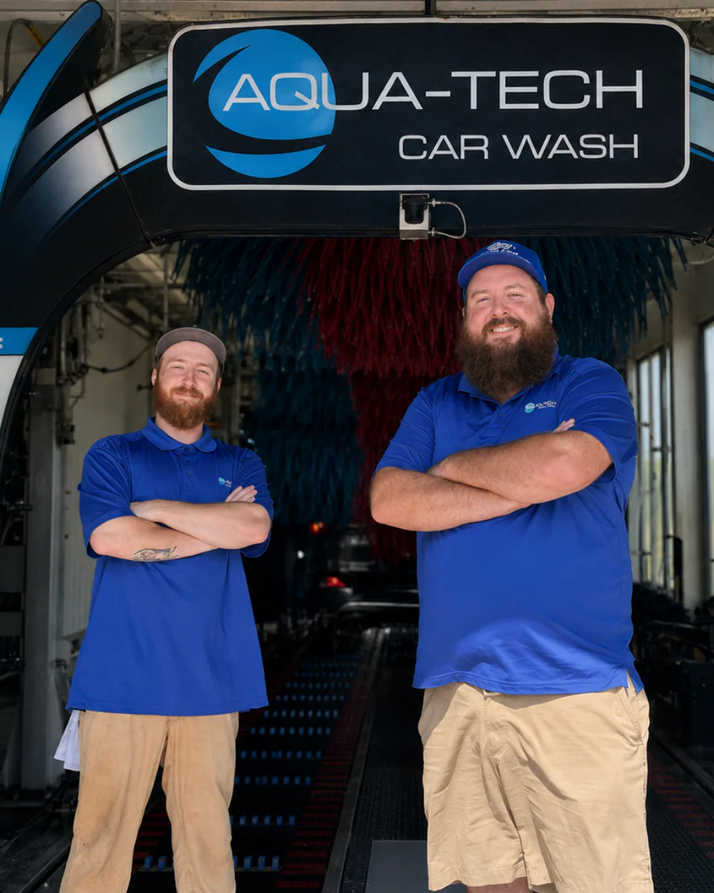Two Aqua-Tech crew members standing at the tunnel entrance under the Aqua-Tech Car Wash sign